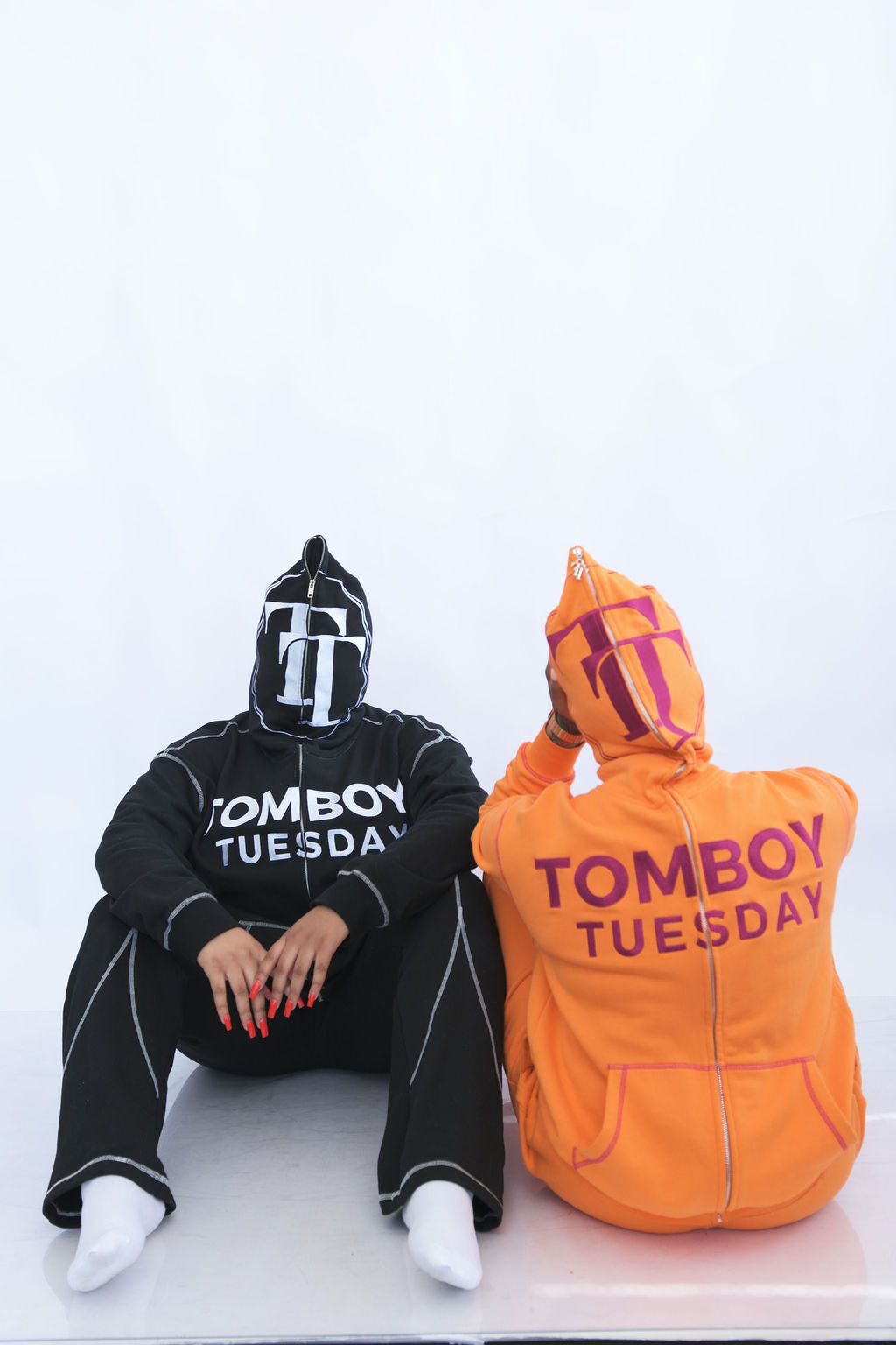 Two people wearing hoodies with 'Tomboy Tuesday' text on a white background